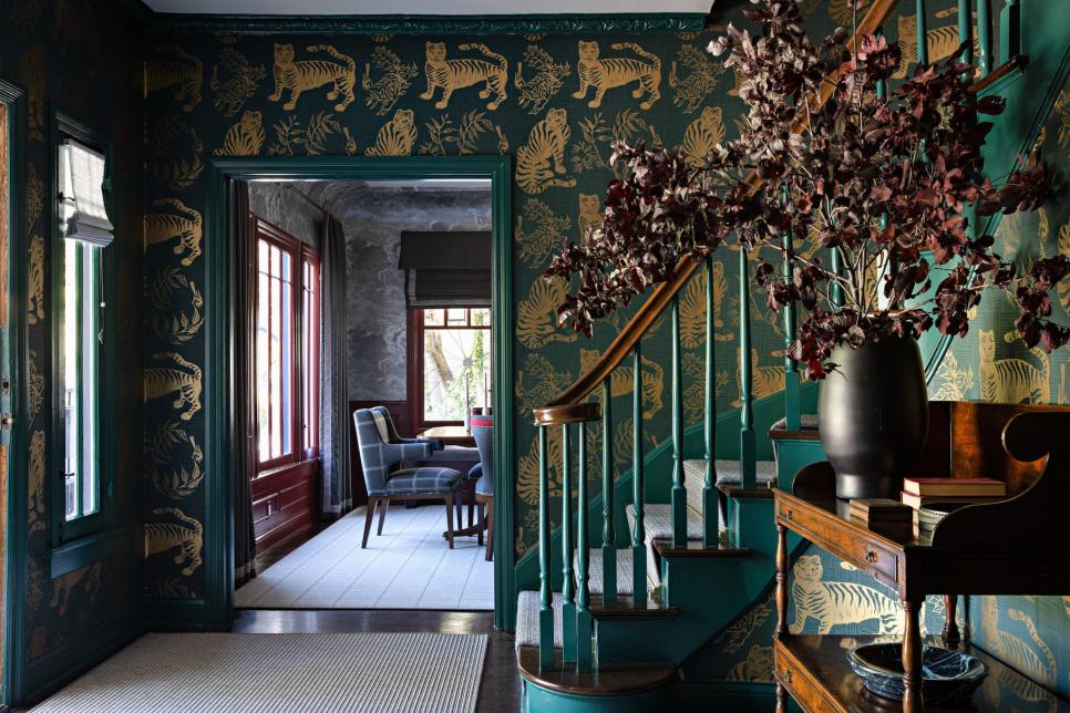 Elegant entryway with teal and gold wallpaper, grand staircase, and floral arrangements.