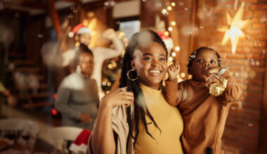 Smiling mother holding her toddler daughter celebrating New Year's Eve at home with bubbles and party horns.