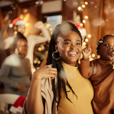 Smiling mother holding her toddler daughter celebrating New Year's Eve at home with bubbles and party horns.
