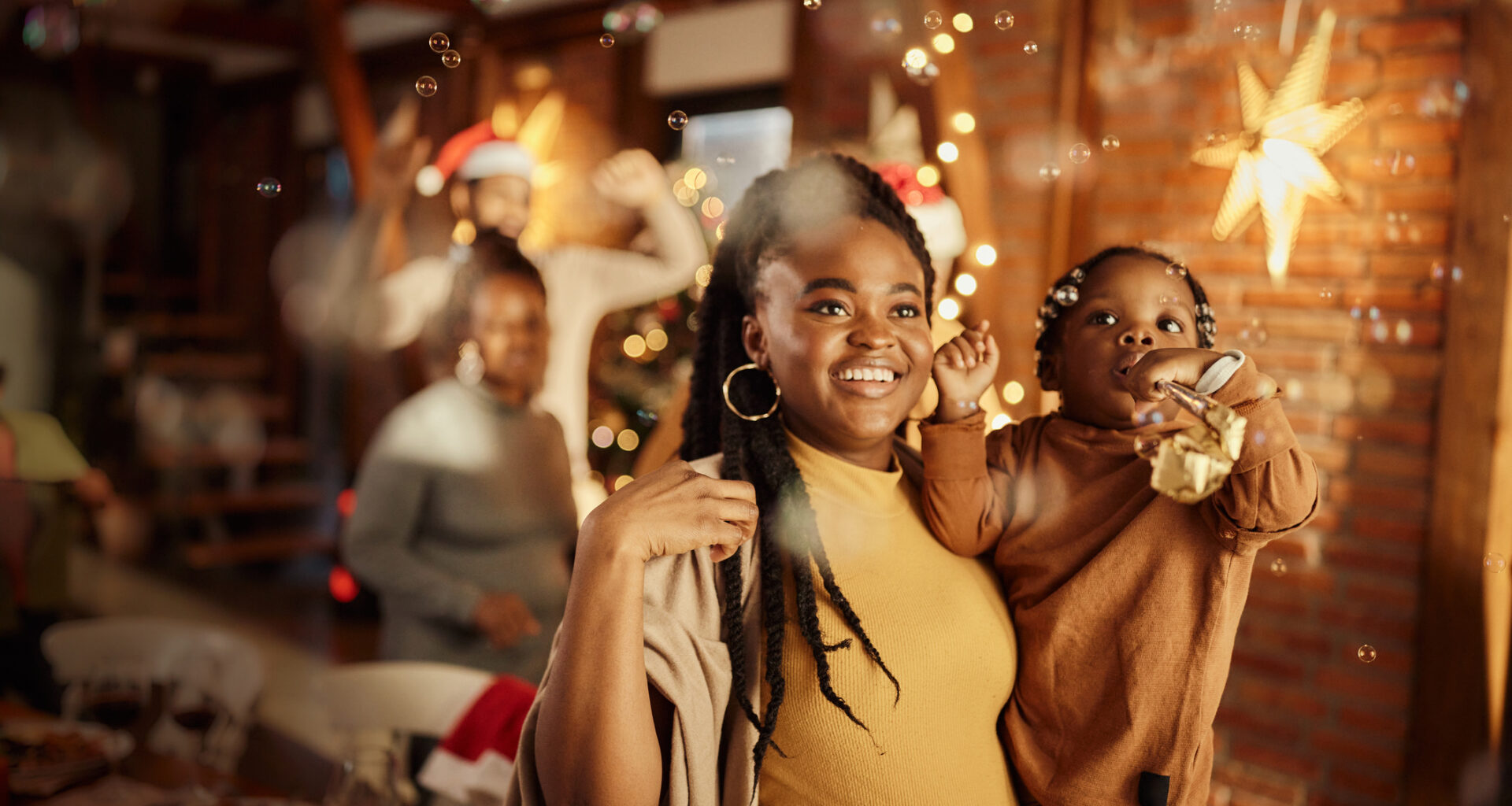 Smiling mother holding her toddler daughter celebrating New Year's Eve at home with bubbles and party horns.
